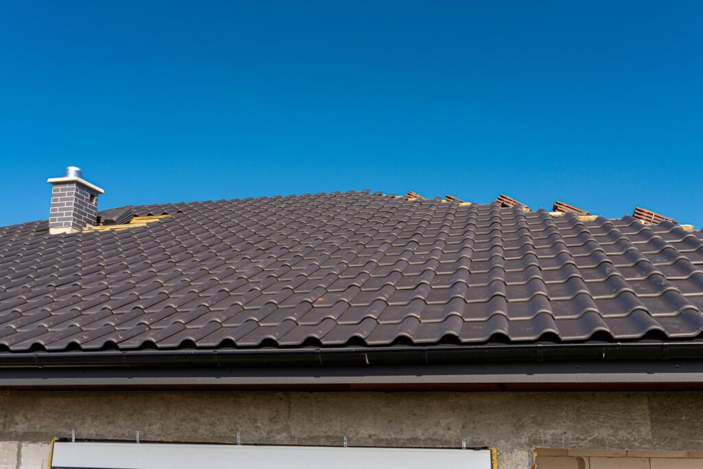 The roof of a single-family house covered with a new ceramic tile in anthracite, against the blue sk