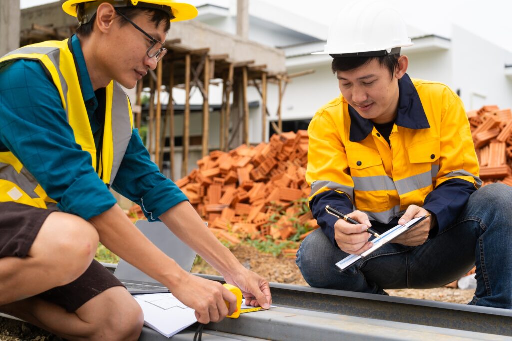 Two men,engaged in conversation, examine steel reinforcements and discuss house structure roofing.